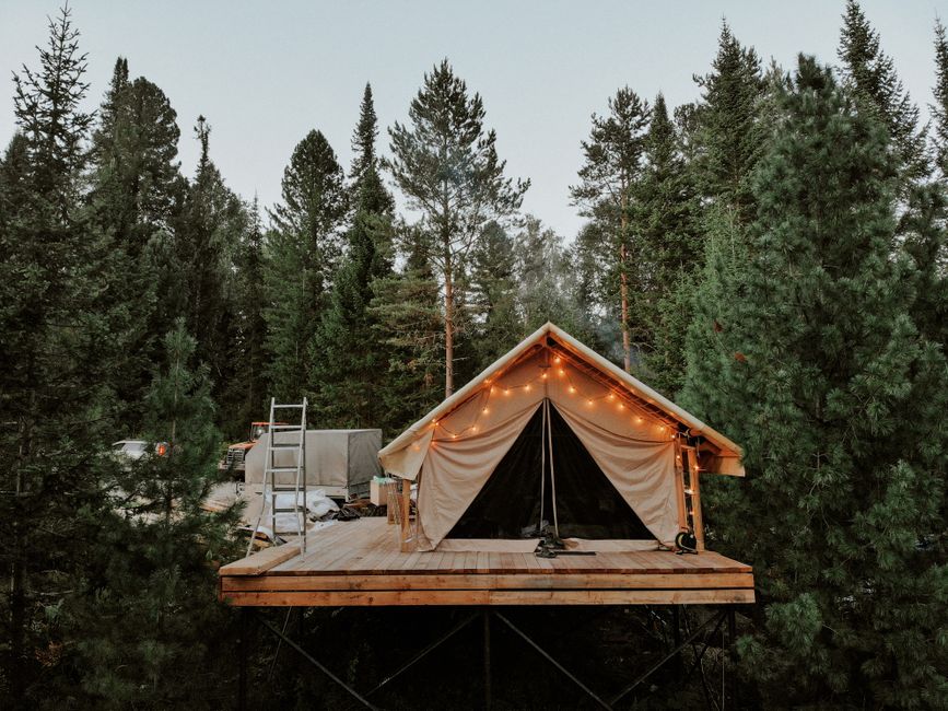 Campsite elevated in forest with fairy lights illuminating a cozy platform tent surrounded by lush trees.