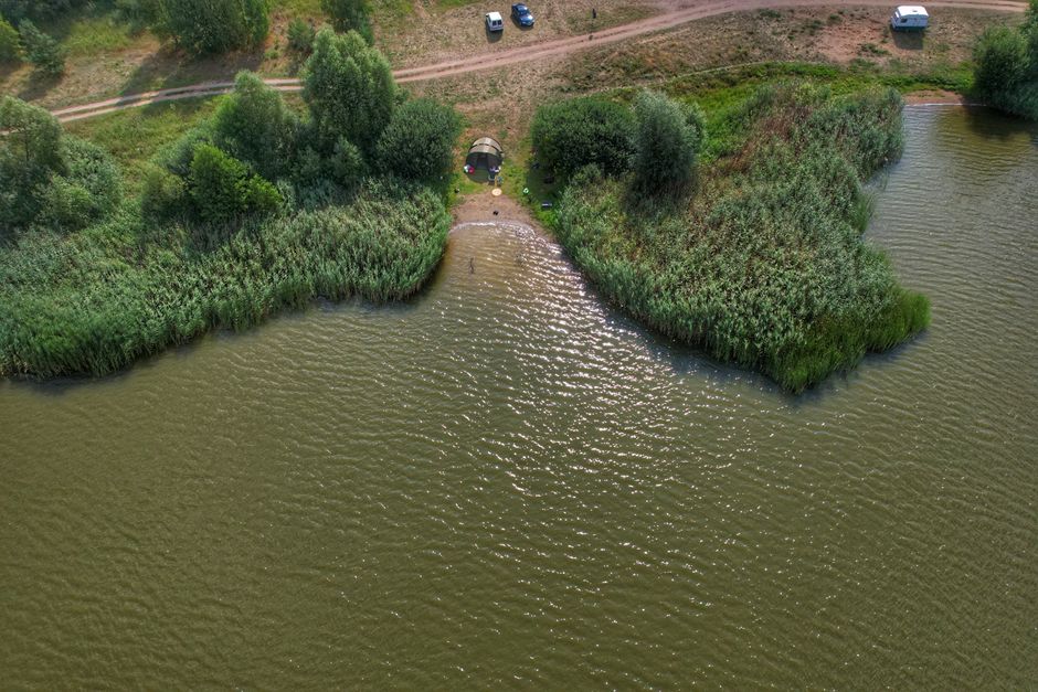 Aerial shot of a tent by a serene lakeside surrounded by lush greenery.